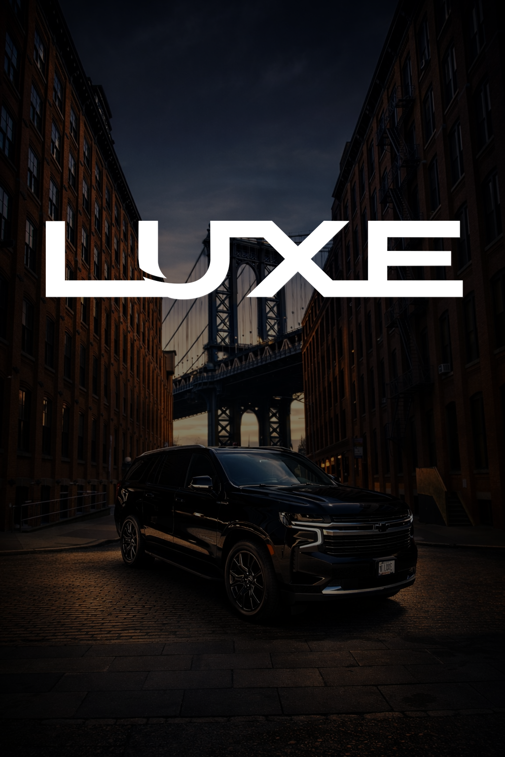 A black SUV parked on a cobblestone street between brick buildings with a bridge in the background at sunset.