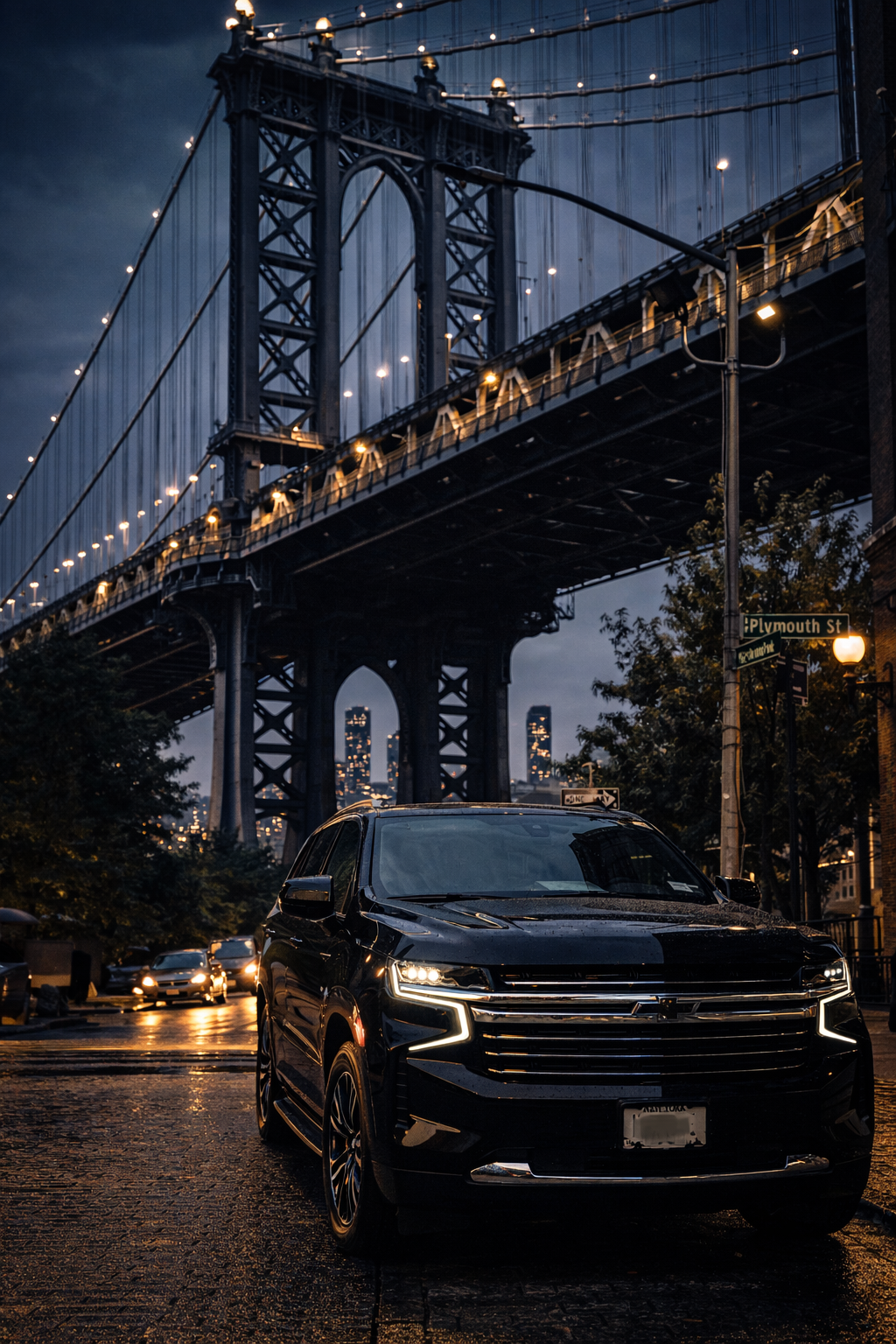 A black Chevrolet SUV parked on a wet city street at dusk under a large suspension bridge with city skyline in the background.