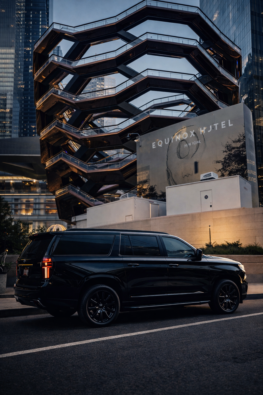 A black SUV parked on the street in front of the Equinox Hotel in New York City, with a modern, multi-level, spiral staircase building and tall skyscrapers in the background during evening.