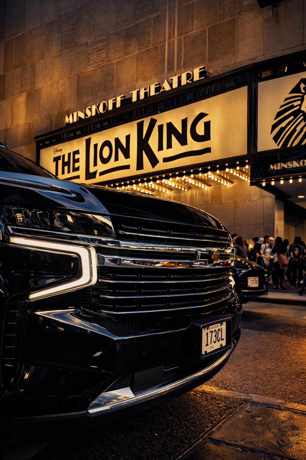 Close-up view of a black luxury car parked in front of the MINSKOFF THEATRE marquee displaying 'The Lion King' in illuminated letters at night, with pedestrians in the background.