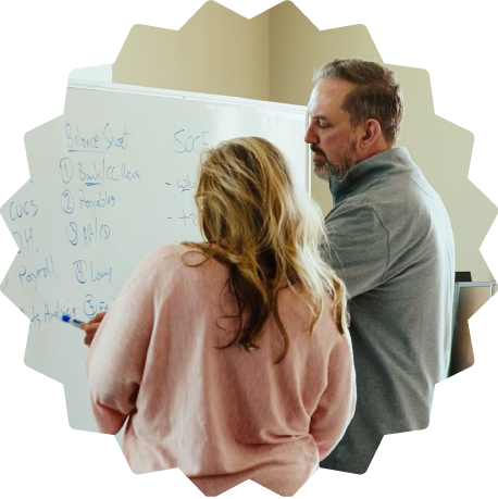 A man and woman standing in front of a whiteboard, discussing and writing on it.