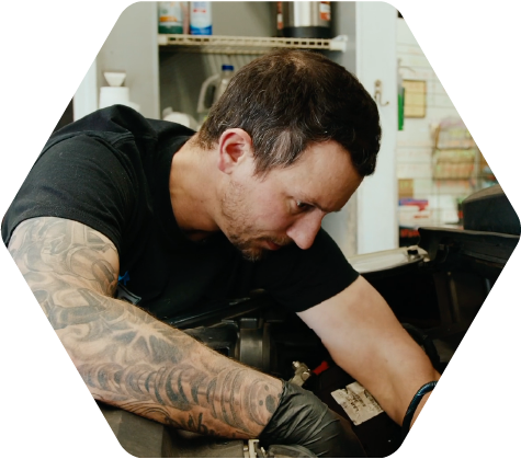 Man with tattoos working on a car engine in a garage or workshop.