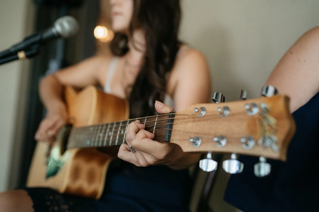 Person playing an acoustic guitar while sitting near a microphone.