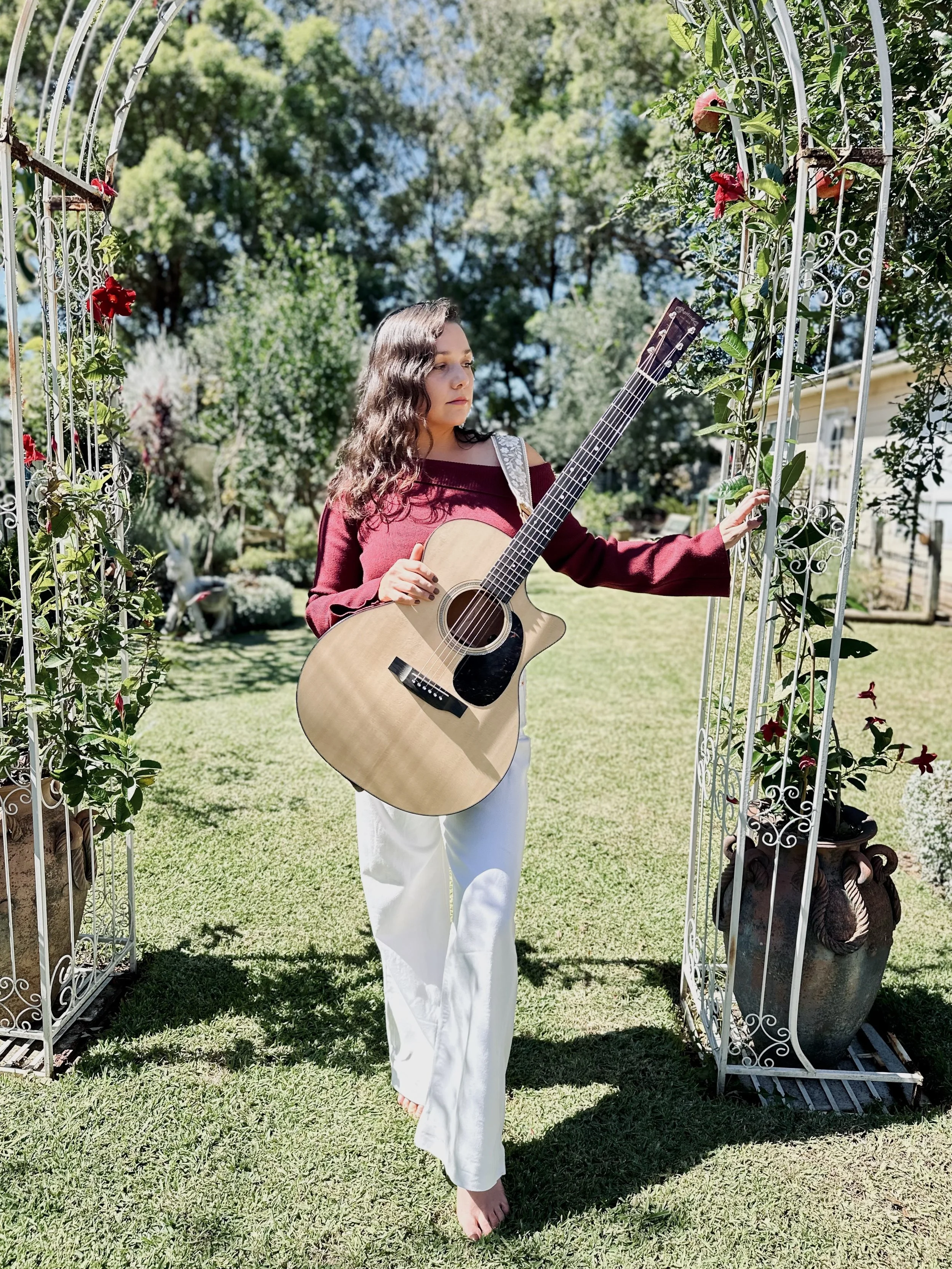 Vocalist 'Dayna' from Acacia Acoustics with her acoustic guitar, playing outdoors in garden with romantic arch-way.