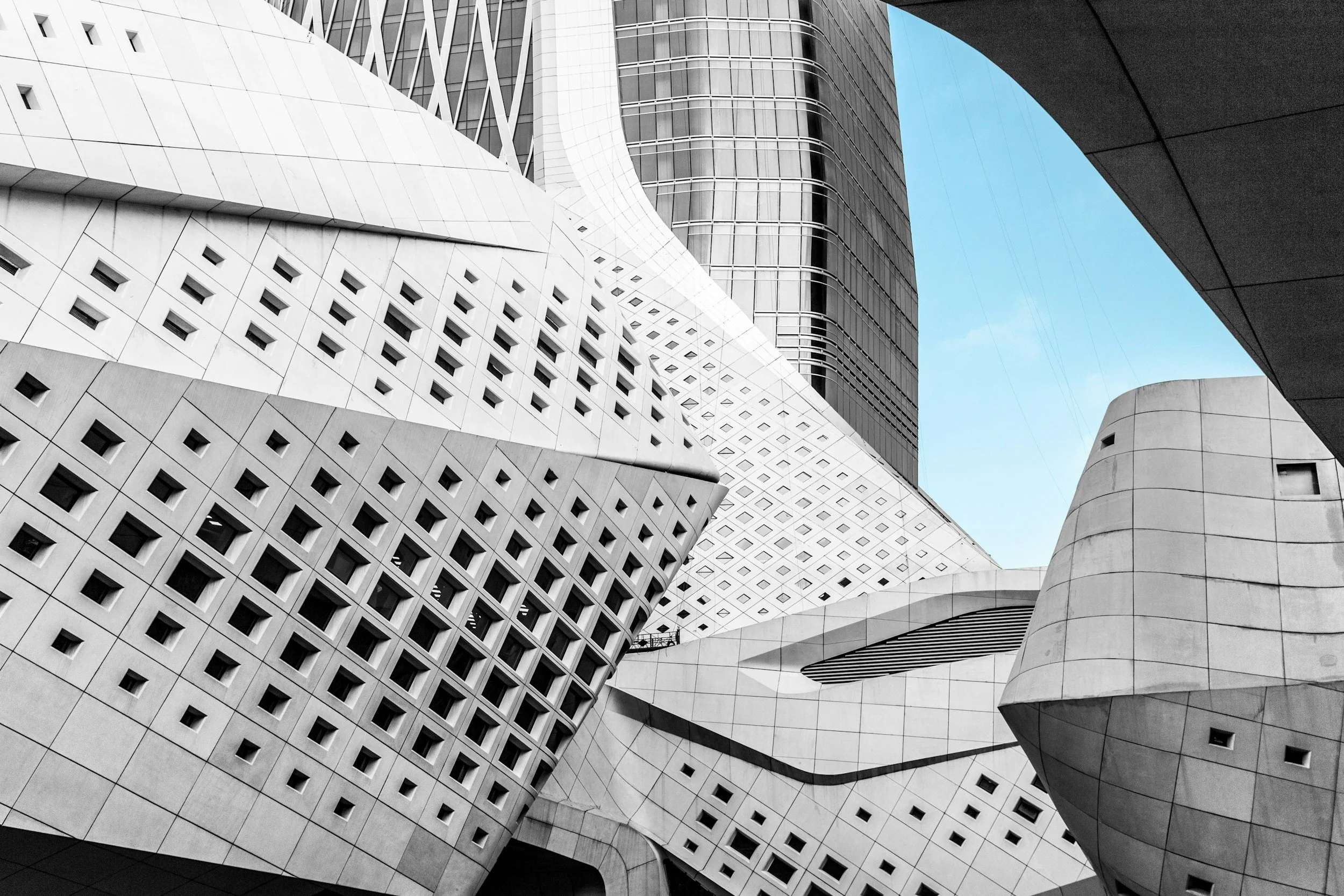 Modern skyscrapers with geometric architectural designs including curved and angular surfaces, expansive windows, and patterned facades against a blue sky.
