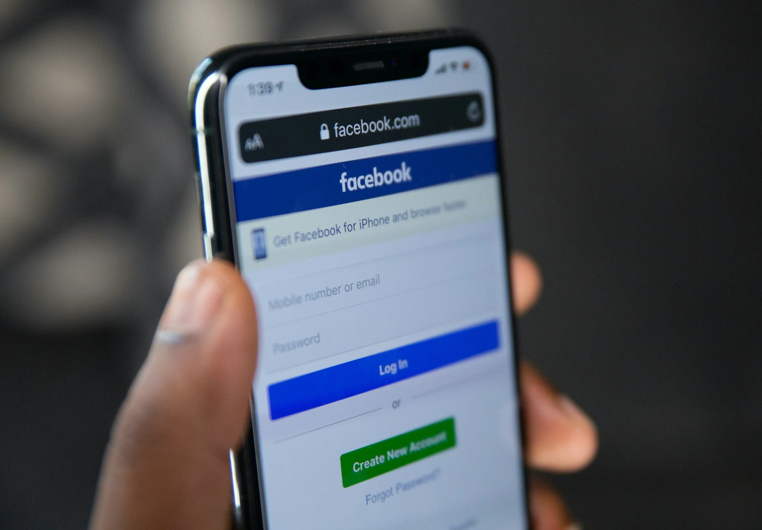 Close-up of a person holding a smartphone displaying the Facebook login page.