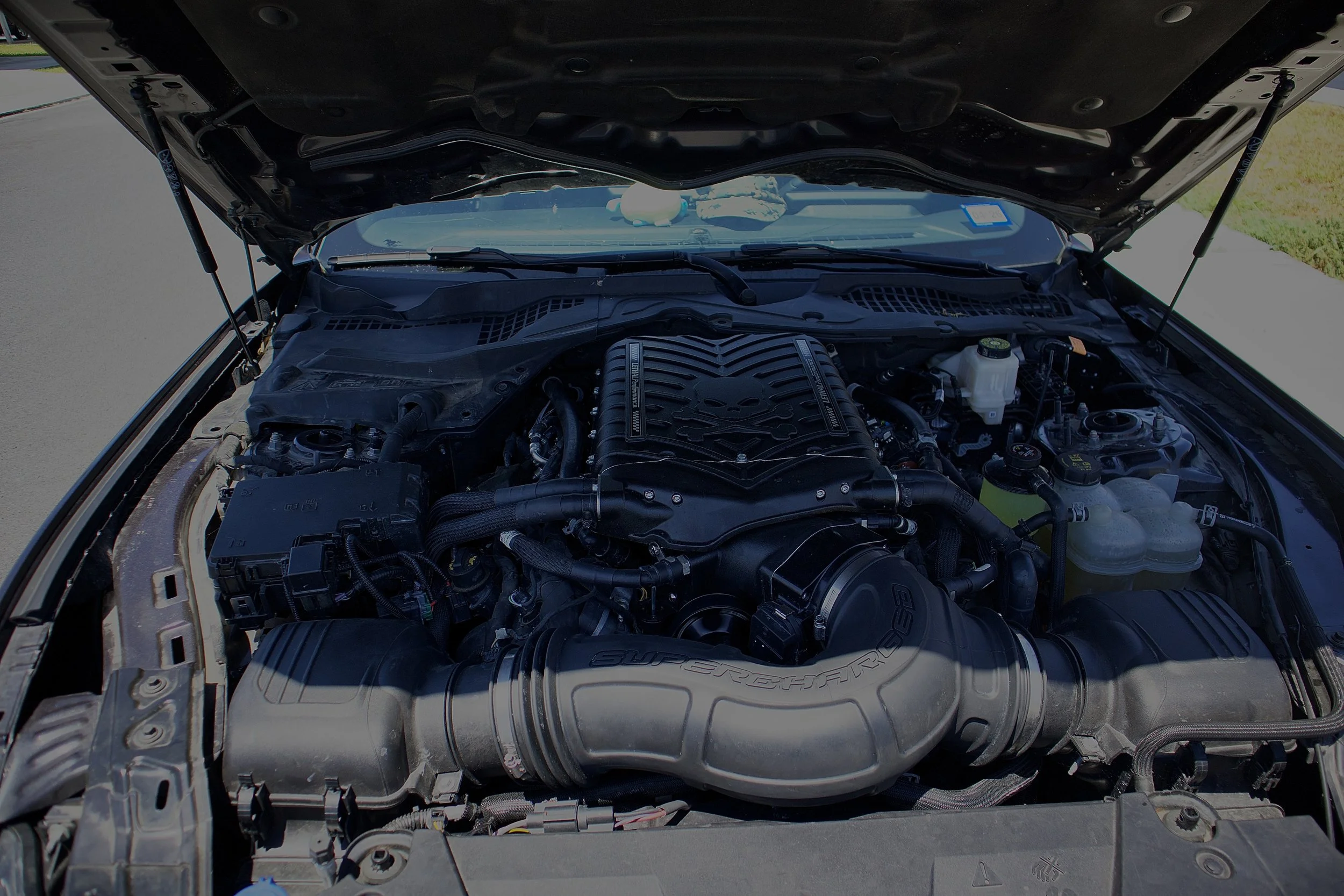 Open car hood showing engine with Supercharged label.