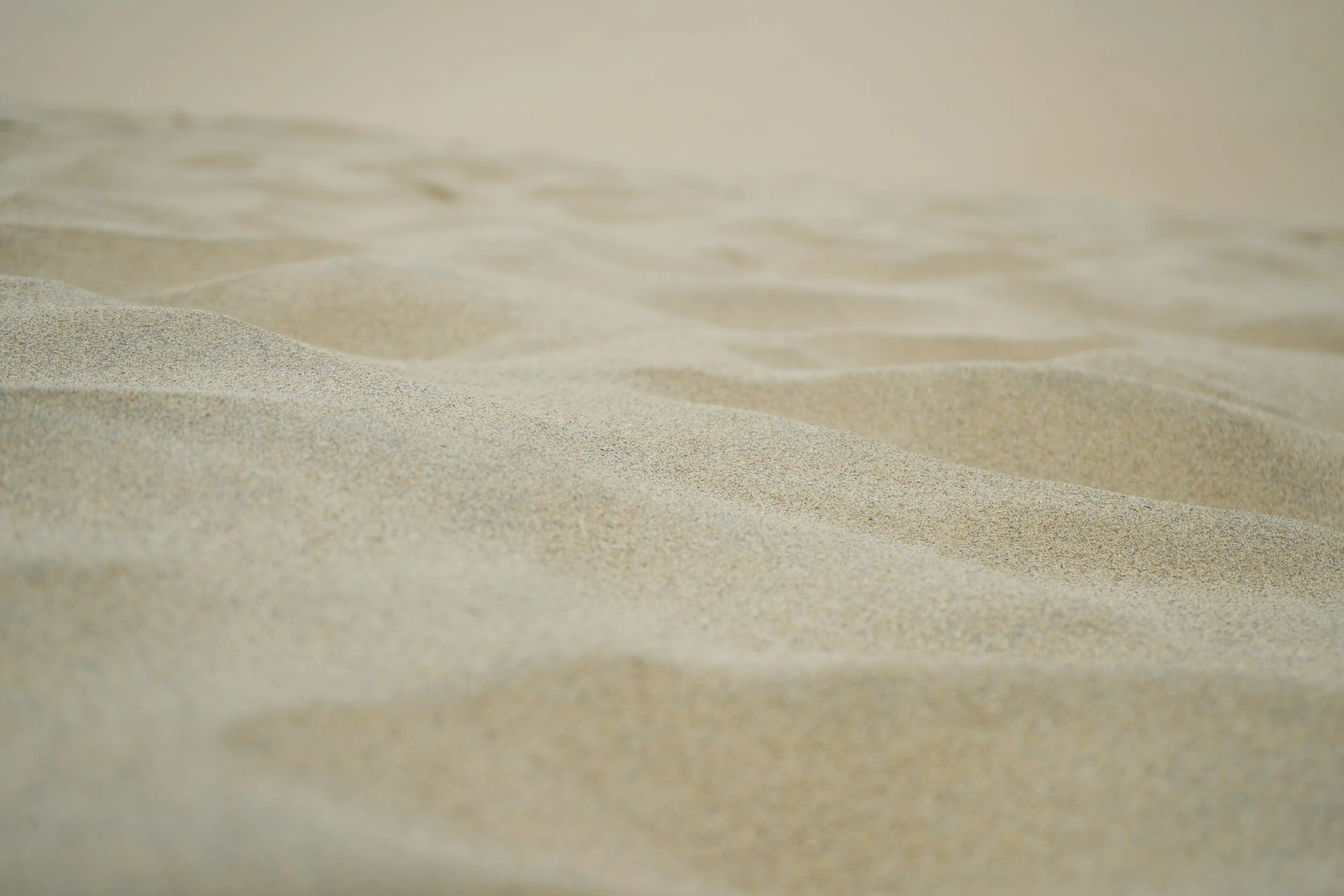 Close-up of sand dunes at the beach with gentle ripples in the sand.