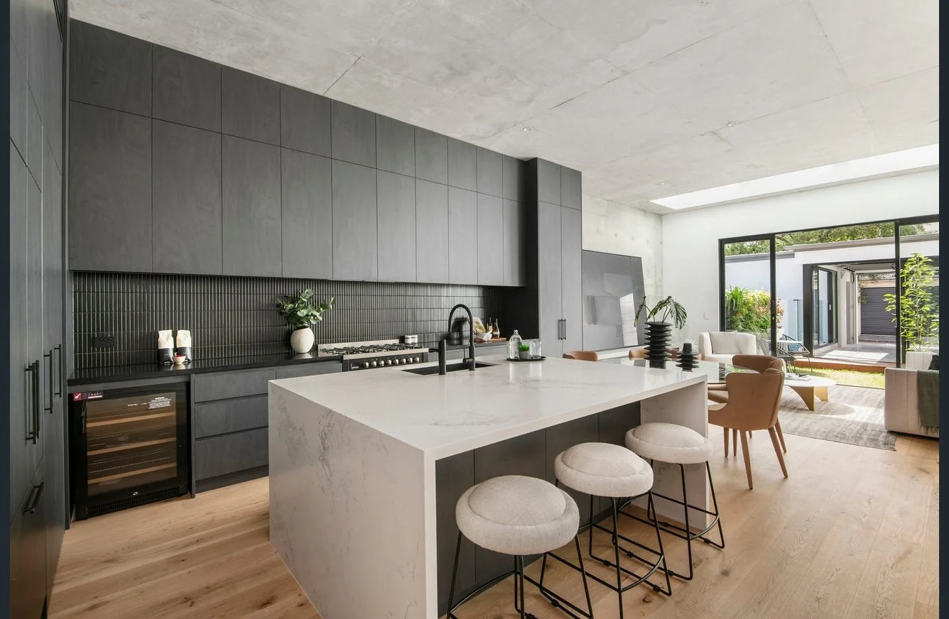 Modern open-concept kitchen and living room with gray cabinets, white island, and large sliding glass doors leading to outdoor patio.