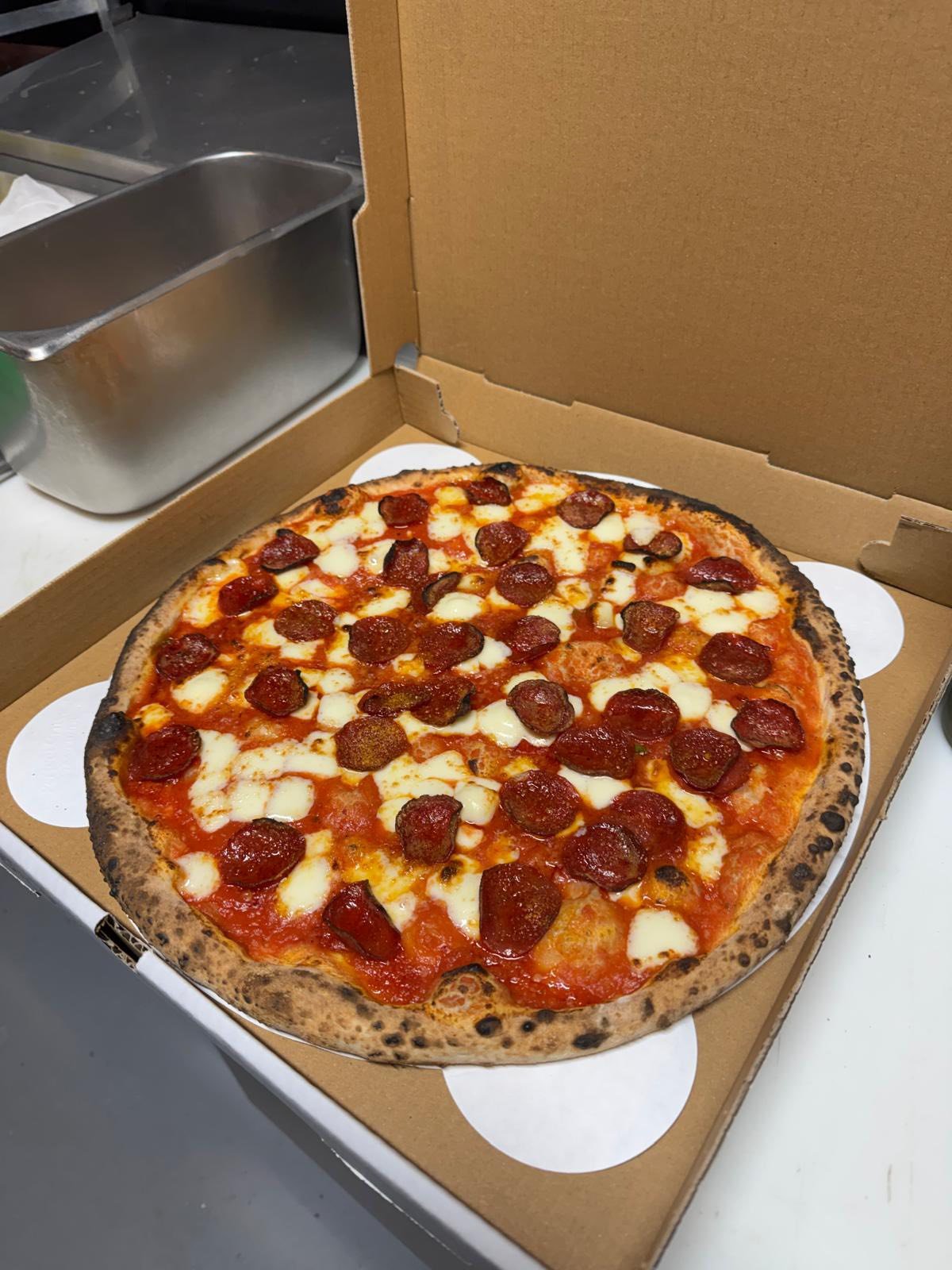 A pepperoni and cheese pizza inside a cardboard pizza box on a white surface.
