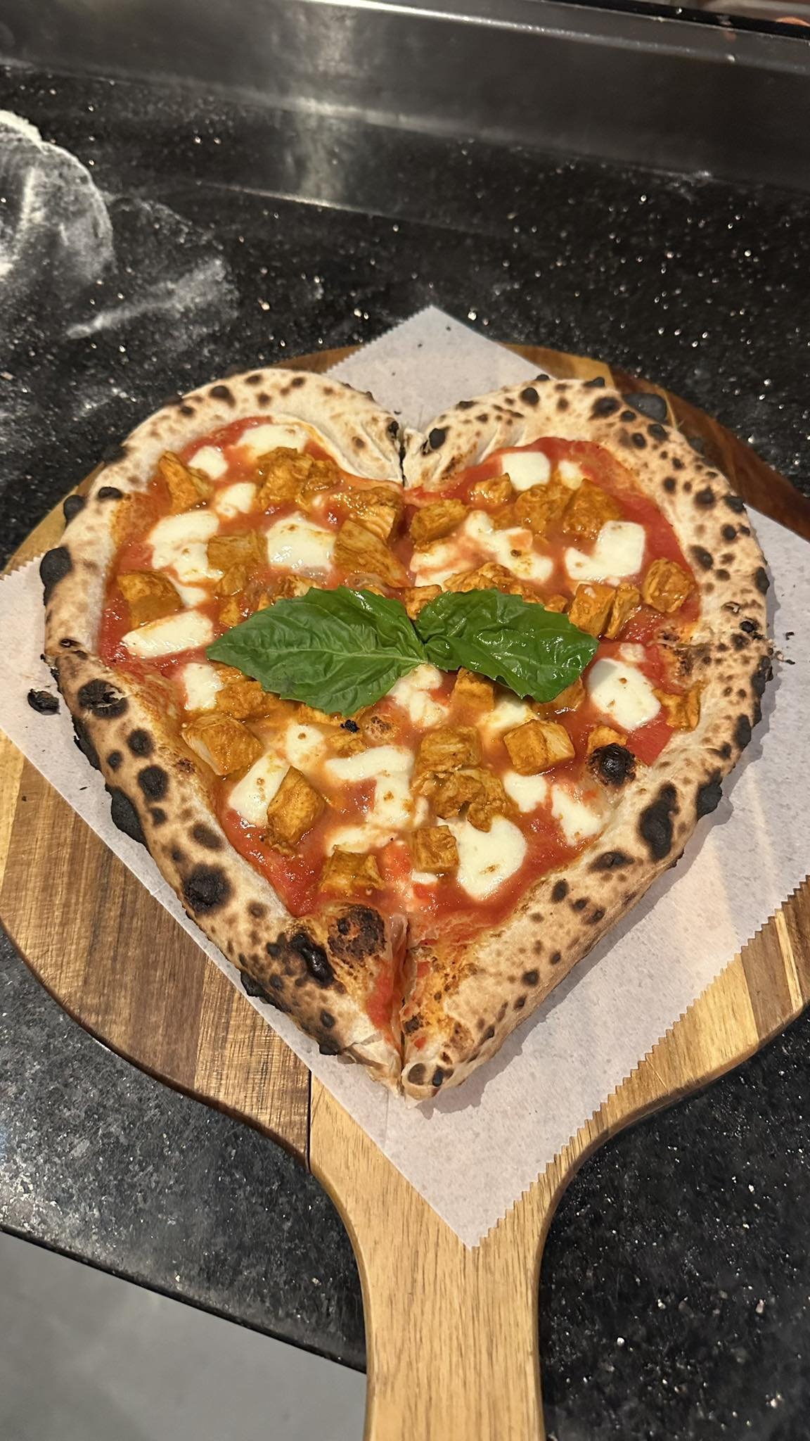 Heart-shaped pizza with tomato sauce, melted mozzarella, chunks of chicken, and basil leaves on top.