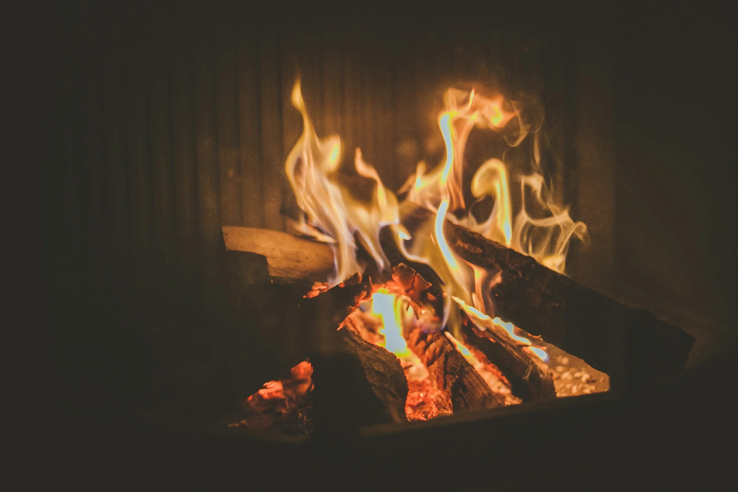 Close-up of a burning fire on logs with orange and yellow flames in darkness.