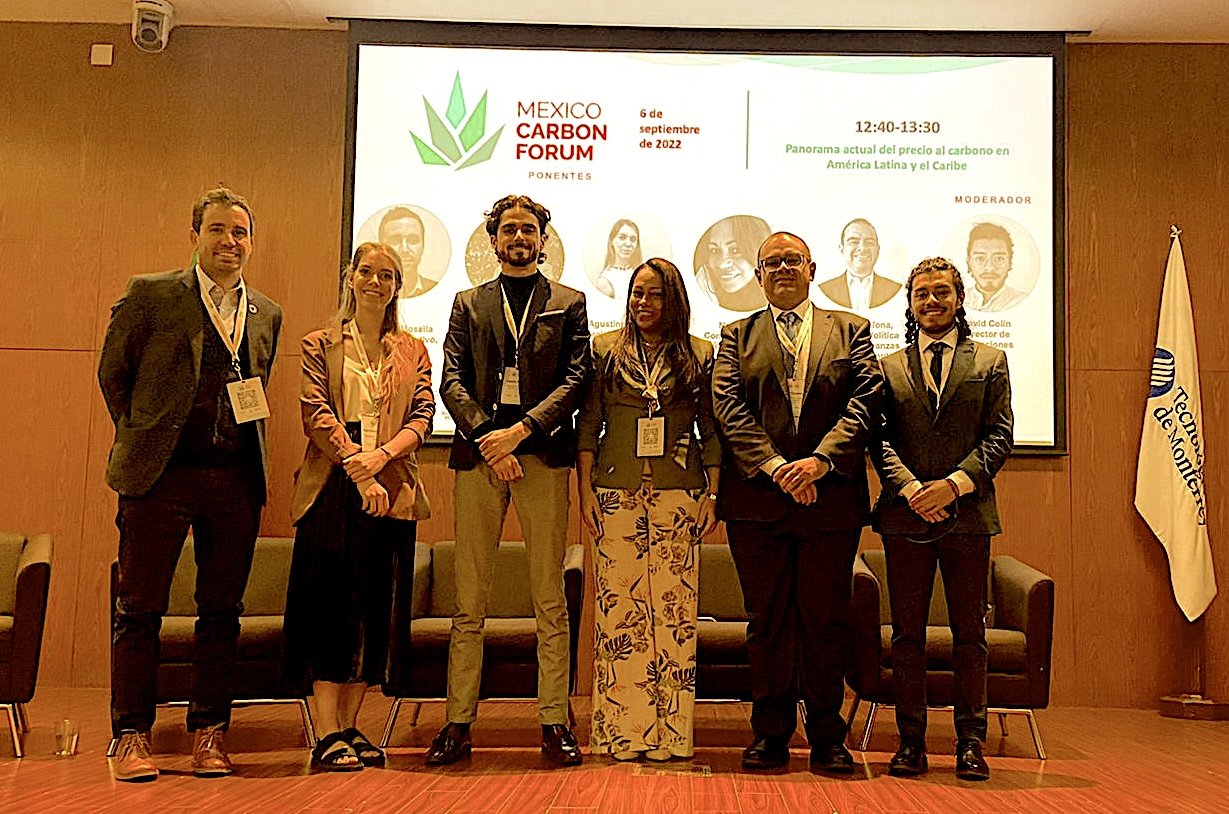Grupo de siete personas en un escenario frente a una pantalla, en un foro sobre carbono en México, noviembre 2022.