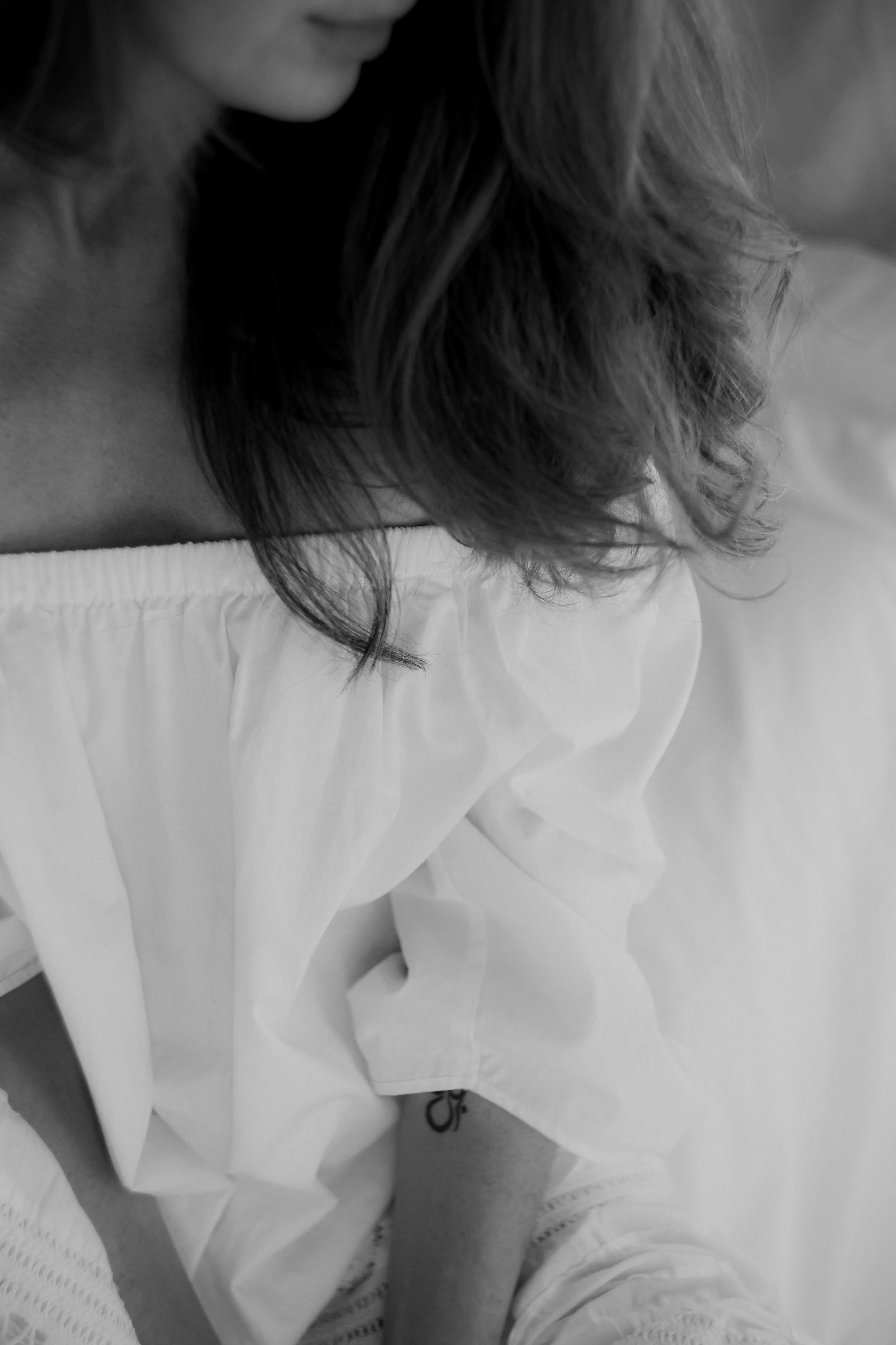 A black and white photo showing a close-up of a woman with wavy hair, wearing a light-colored shirt, sitting and undressing.