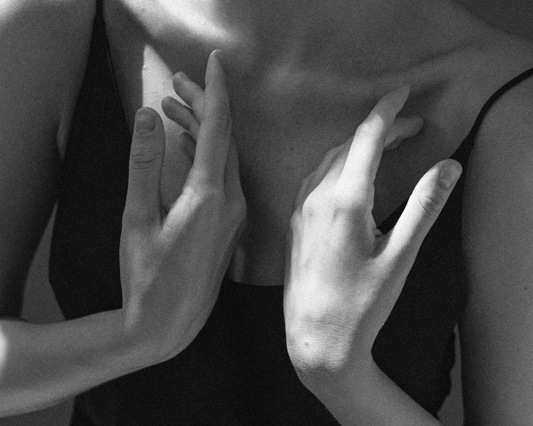 Close-up of a person wearing a black spaghetti strap top, with their hands positioned on their chest.