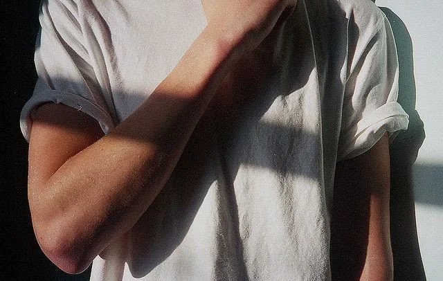 Close-up of a person wearing a white t-shirt with rolled-up sleeves, with shadow falling across their chest and arm.
