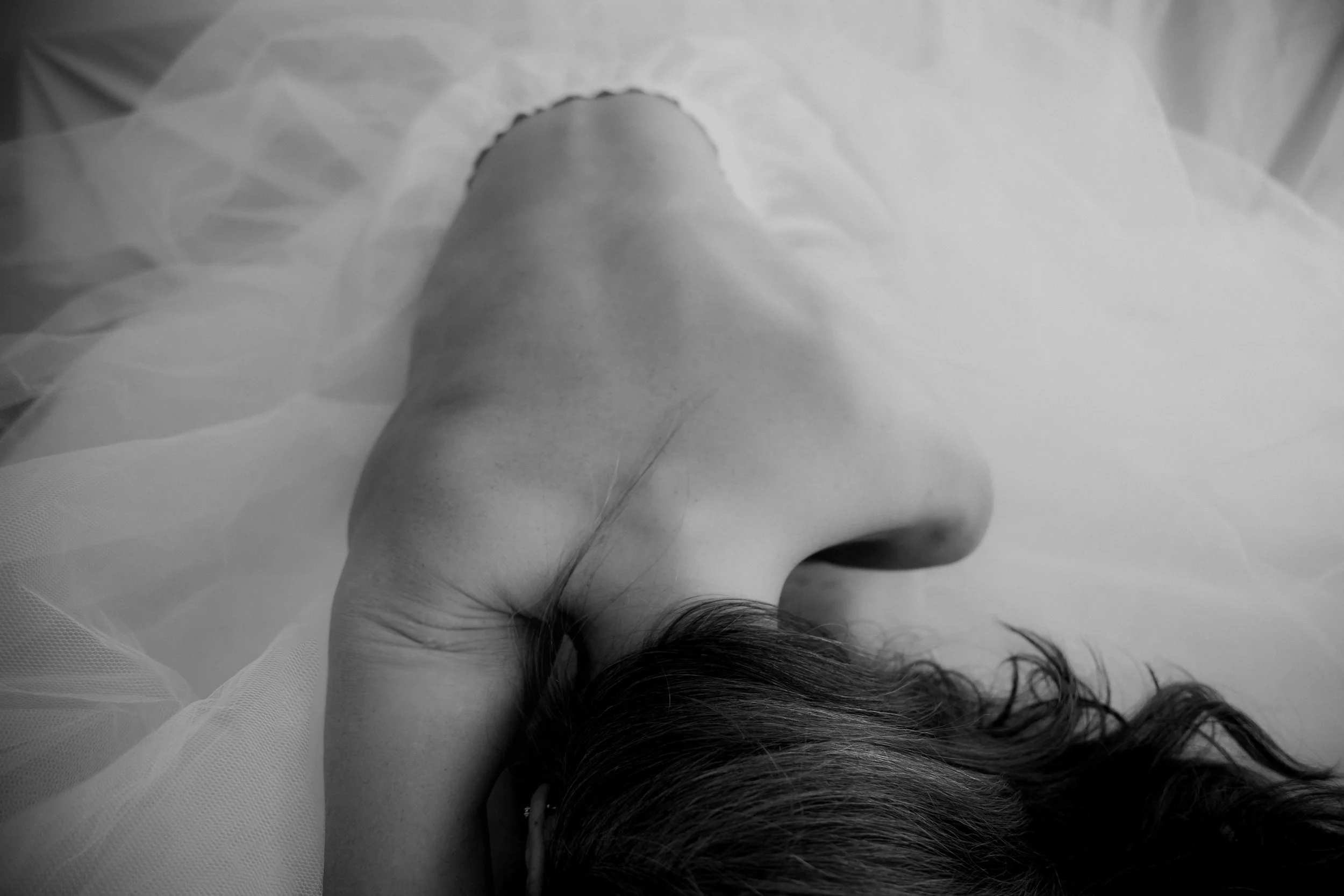 A black and white photograph of a woman's face lying on a surface with her eyes closed, hair spread out around her head.