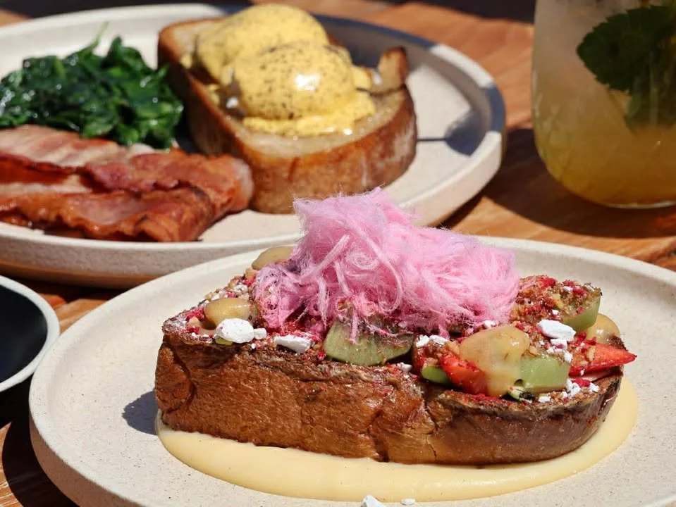 A plate with a cooked beef steak topped with pink cotton candy and vegetables, with additional breakfast items including spinach and bacon in the background.