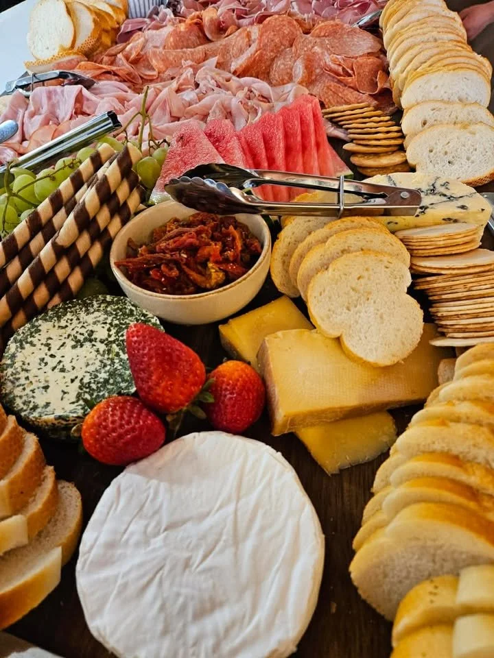 Assorted charcuterie board with sliced bread, cheese, grapes, strawberries, sliced watermelon, and cured meats.