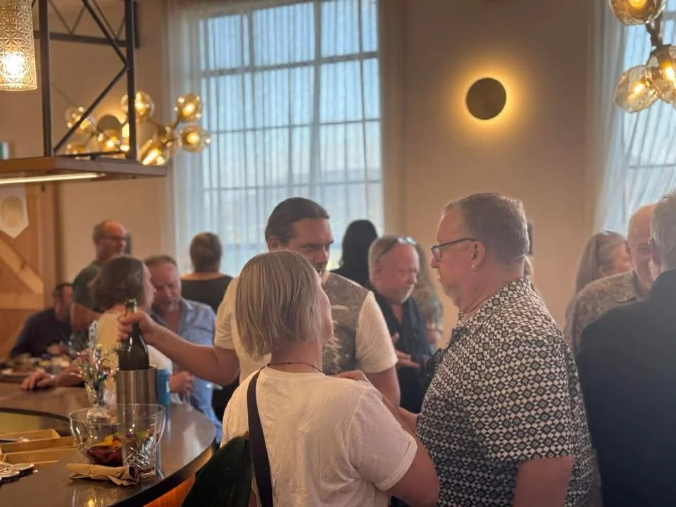 People socializing in a lively indoor space with modern lighting fixtures and large windows.