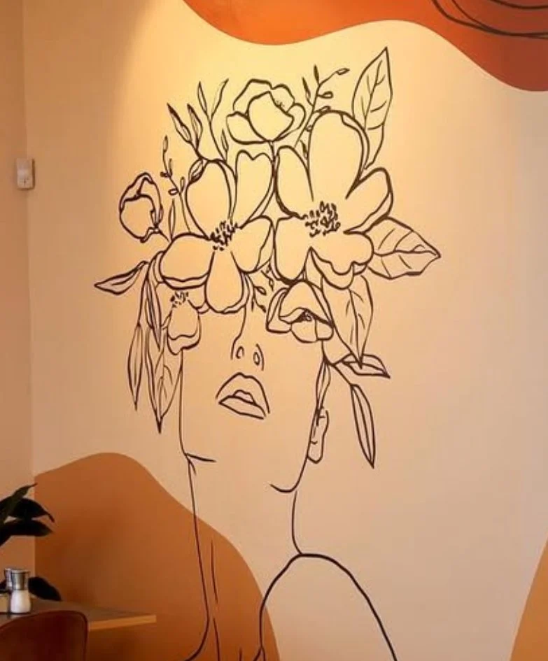 Wall art of a line drawing of a woman's face with her eyes closed and lips slightly parted, with large flowers and leaves as her hair, in a minimalistic style.