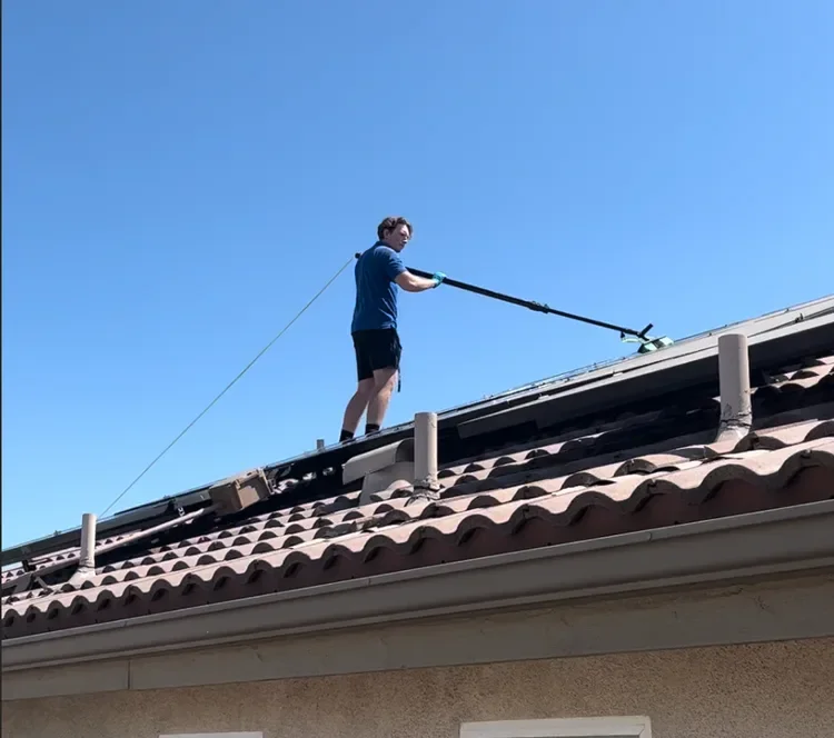 A window washer cleaning solar panels on top of a roof using a waterfed pole.