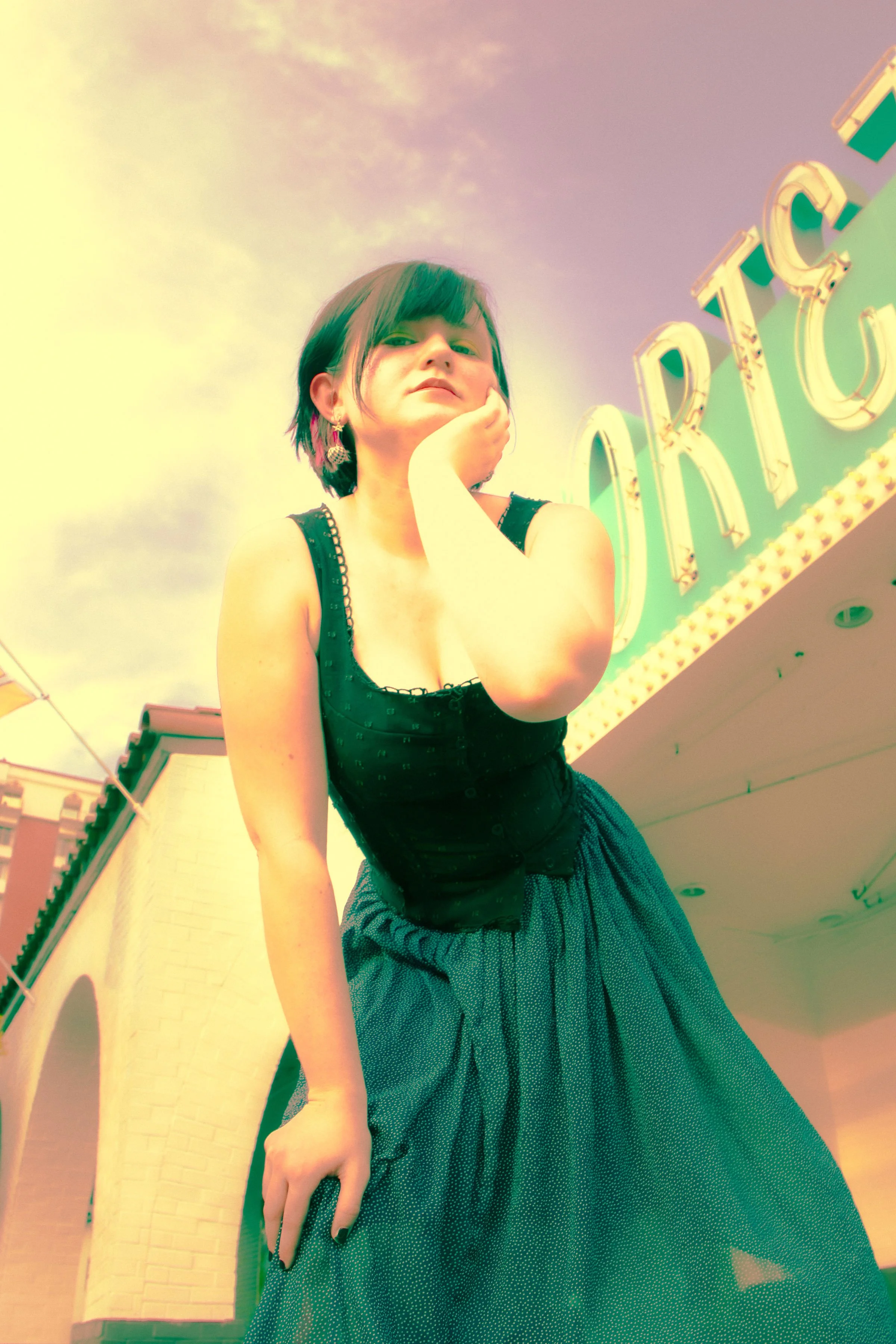 A woman with short dark hair and earrings posing outdoors near a building and a bright sign that says 'CIRCUS'.