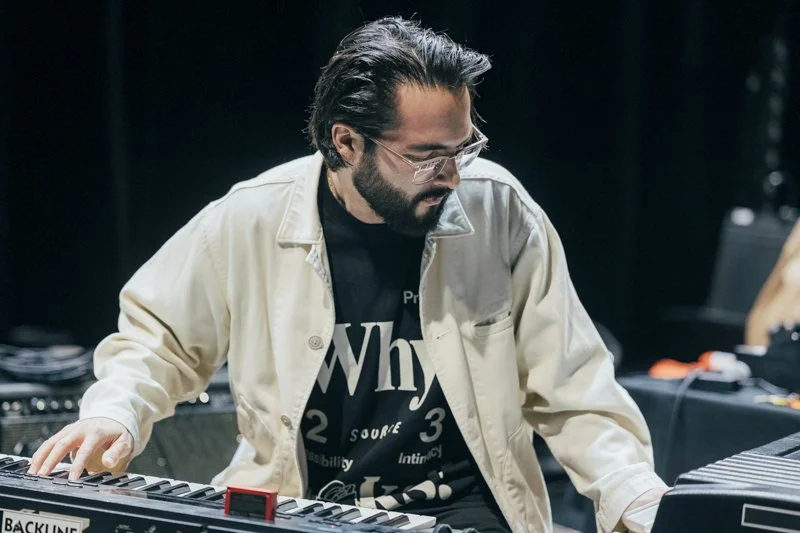 Man with glasses and a beard playing a keyboard on stage.