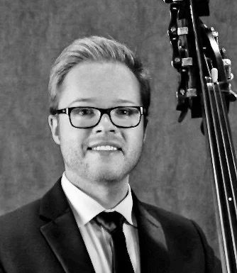 Black and white portrait of a man in formal attire with glasses, holding a double bass.