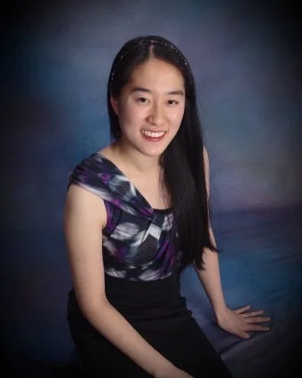 Portrait of a young woman with long black hair, wearing a patterned dress, smiling, posed against a colorful studio background.