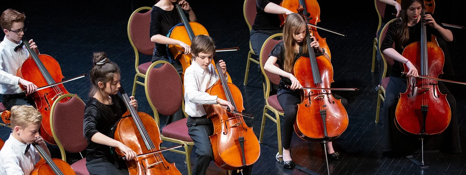 Orchestra of children playing cellos on stage during a performance.