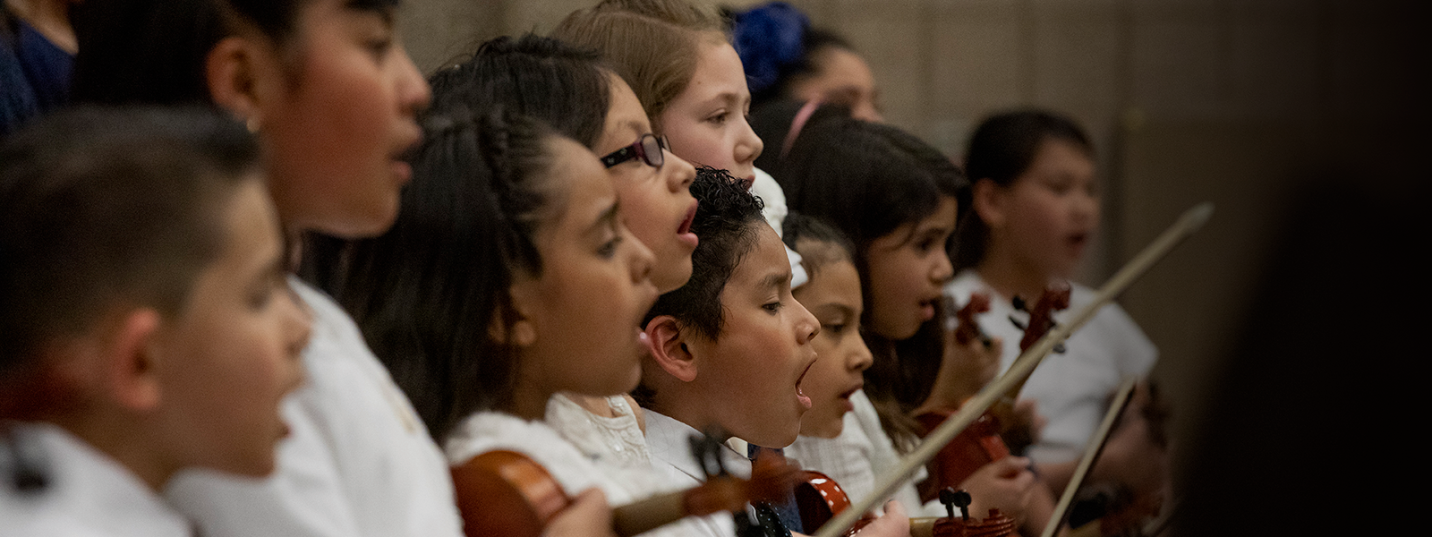 Children singing and playing violins in a choir or music class.