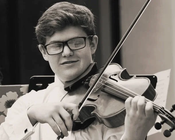 A young man wearing glasses playing a violin.