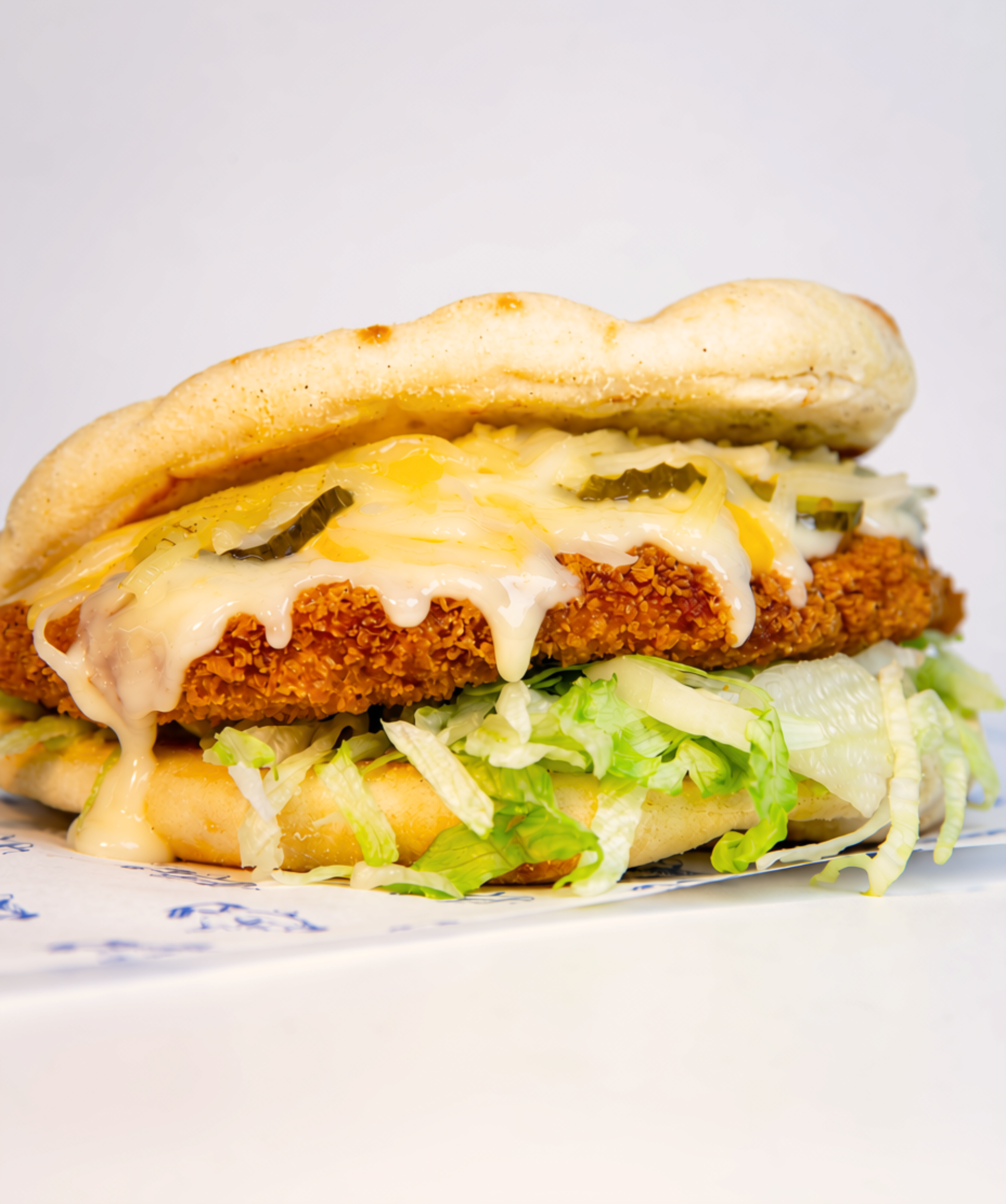Close-up of a fried chicken sandwich with melted cheese, shredded lettuce, and pickles in a bun.