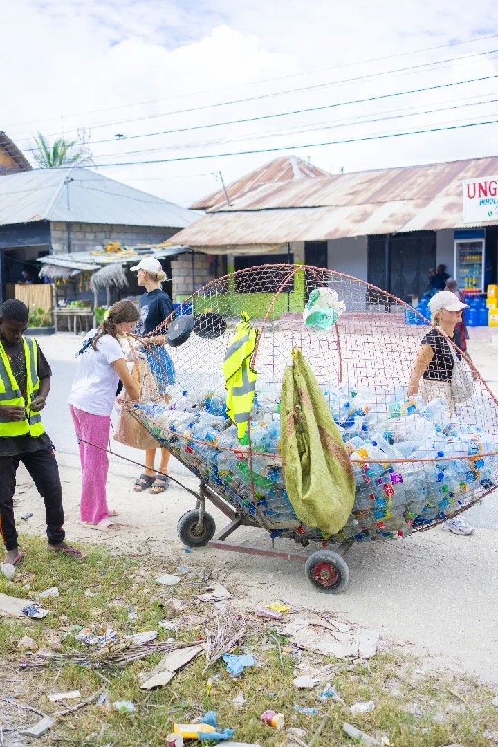 People collecting plastic bottles and recyclables from a cart in a rural area.