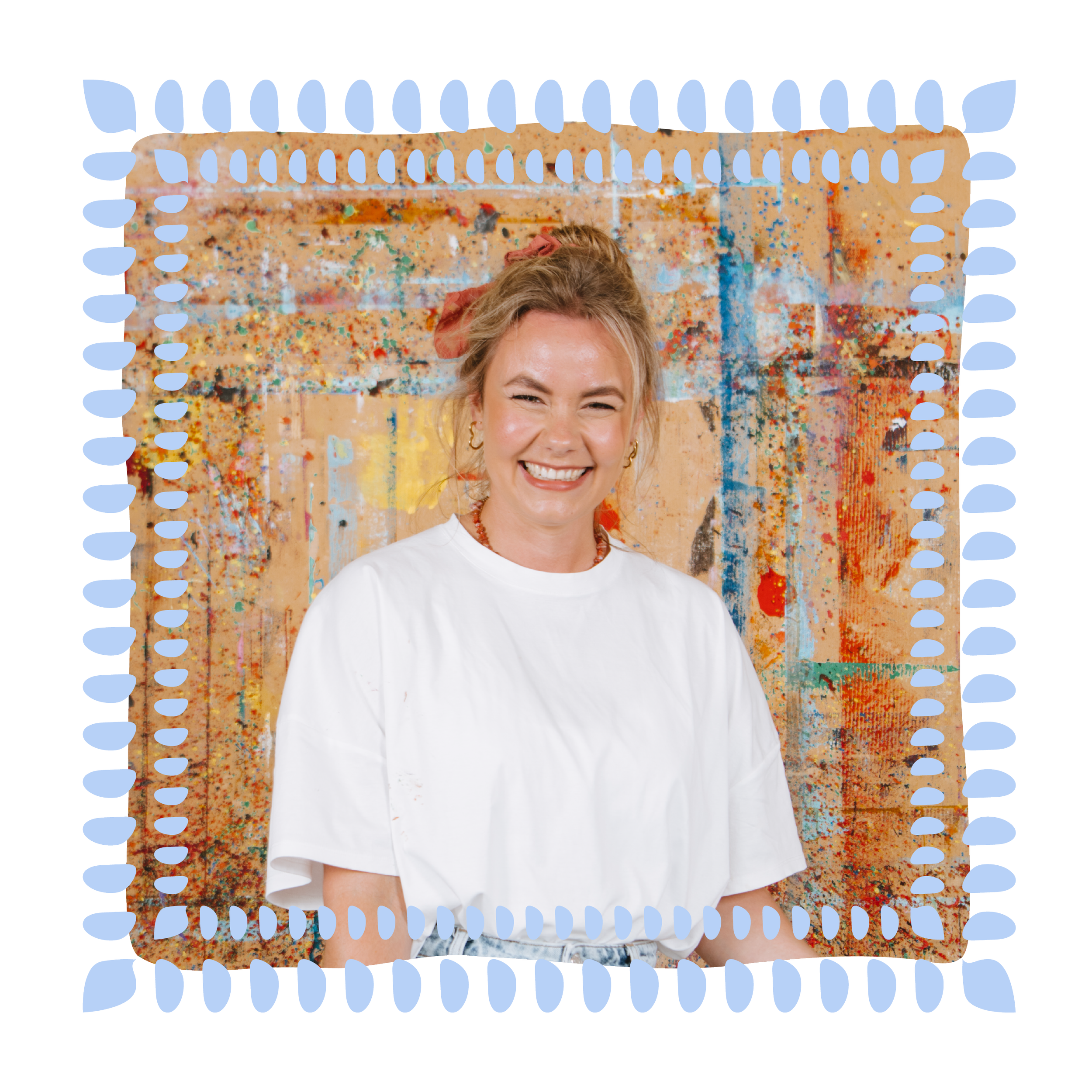 Smiling young woman with blonde hair tied in a pink scrunchie, standing in front of an abstract colorful painting.
