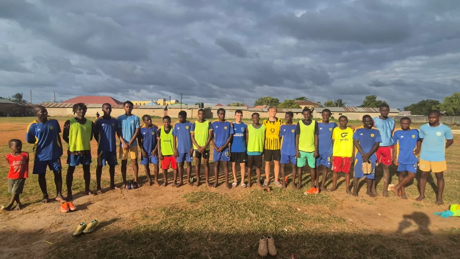 Group of young soccer players and coaches standing on a field, posing for a photo during daytime under a cloudy sky.