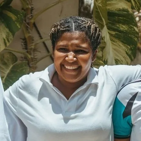 A woman smiling outdoors with trees in the background, wearing a light-colored polo shirt.