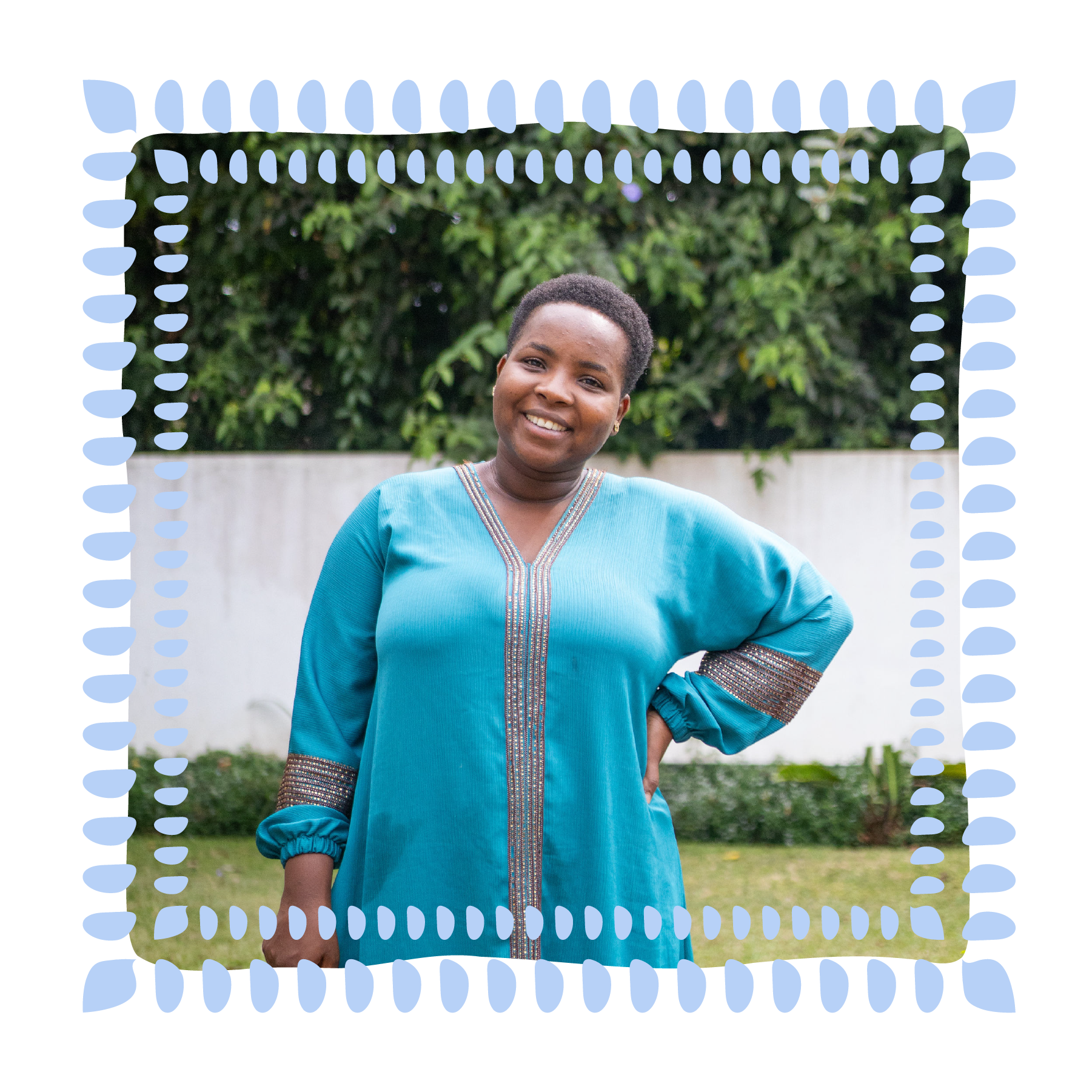 A smiling woman with short hair wearing a traditional blue dress with intricate embroidery, standing outdoors with greenery in the background.
