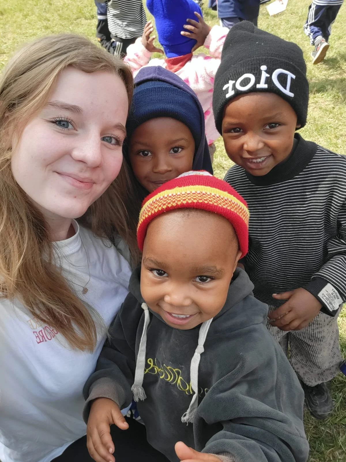 Group of children and a young woman outdoors, smiling for a selfie.