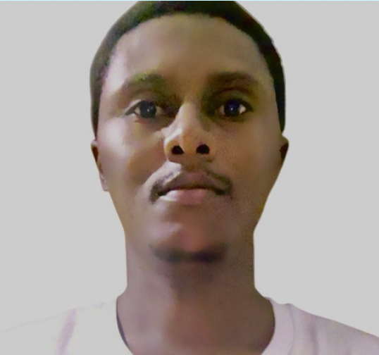 A young man with short hair and a mustache looking straight at the camera, wearing a white shirt.