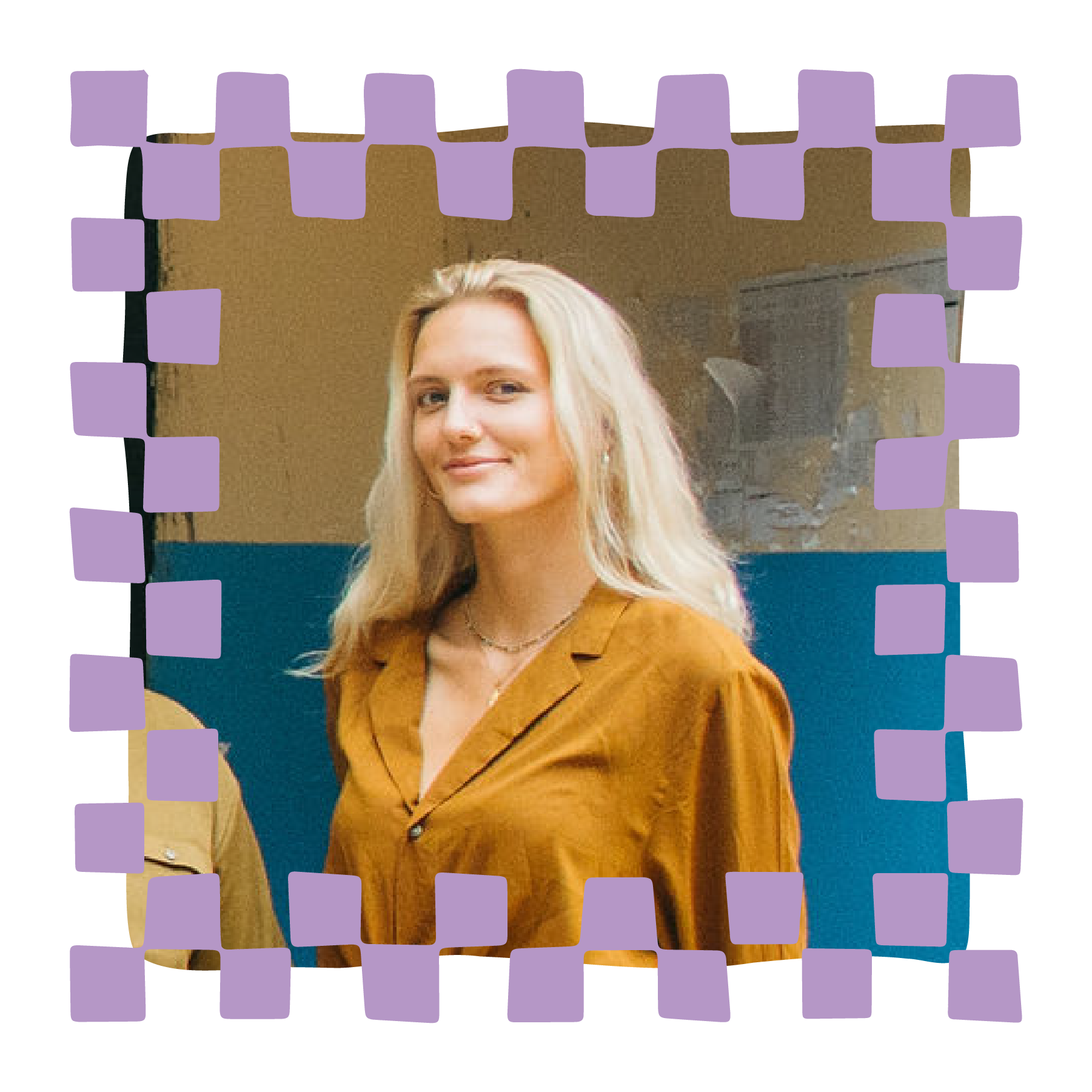 A young woman with blonde hair wearing a mustard yellow blazer and white top, smiling indoors against a beige wall.