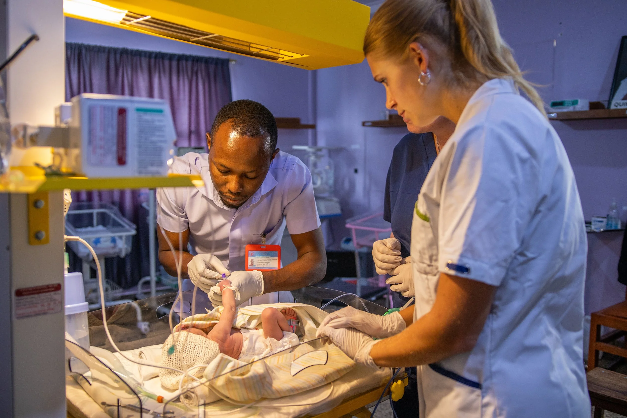 Medical professionals in a neonatal intensive care unit attending to a newborn baby in an incubator.