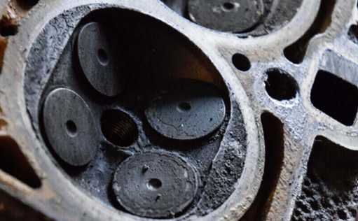 Close-up of a damaged engine cylinder head with visible piston chambers.