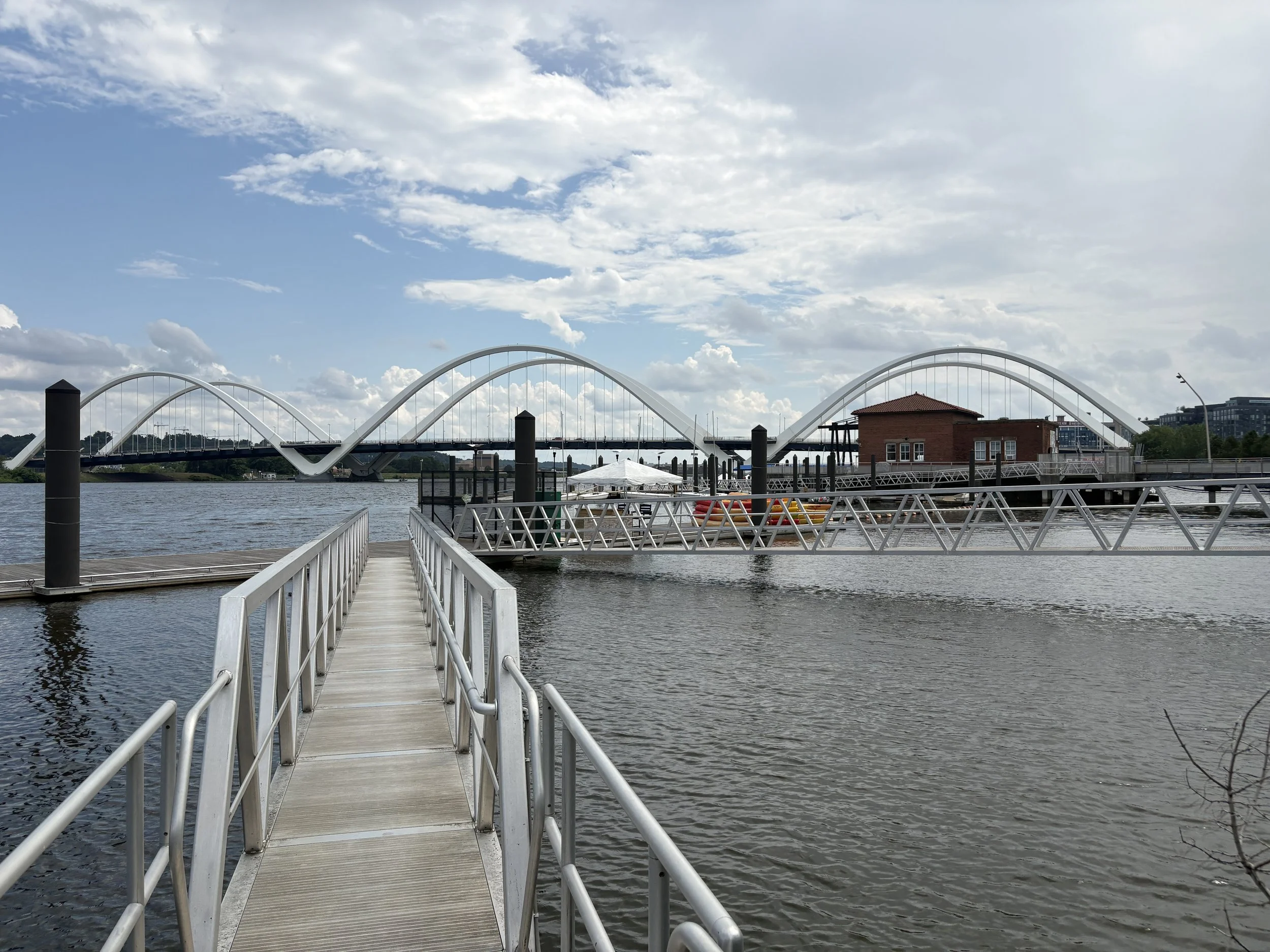 Frederick Douglass Memorial Bridge across the Anacostia River, with the red brick waterfront building and marina in the foreground, photographed by Twan Woods in Washington, D.C., July 9, 2026.