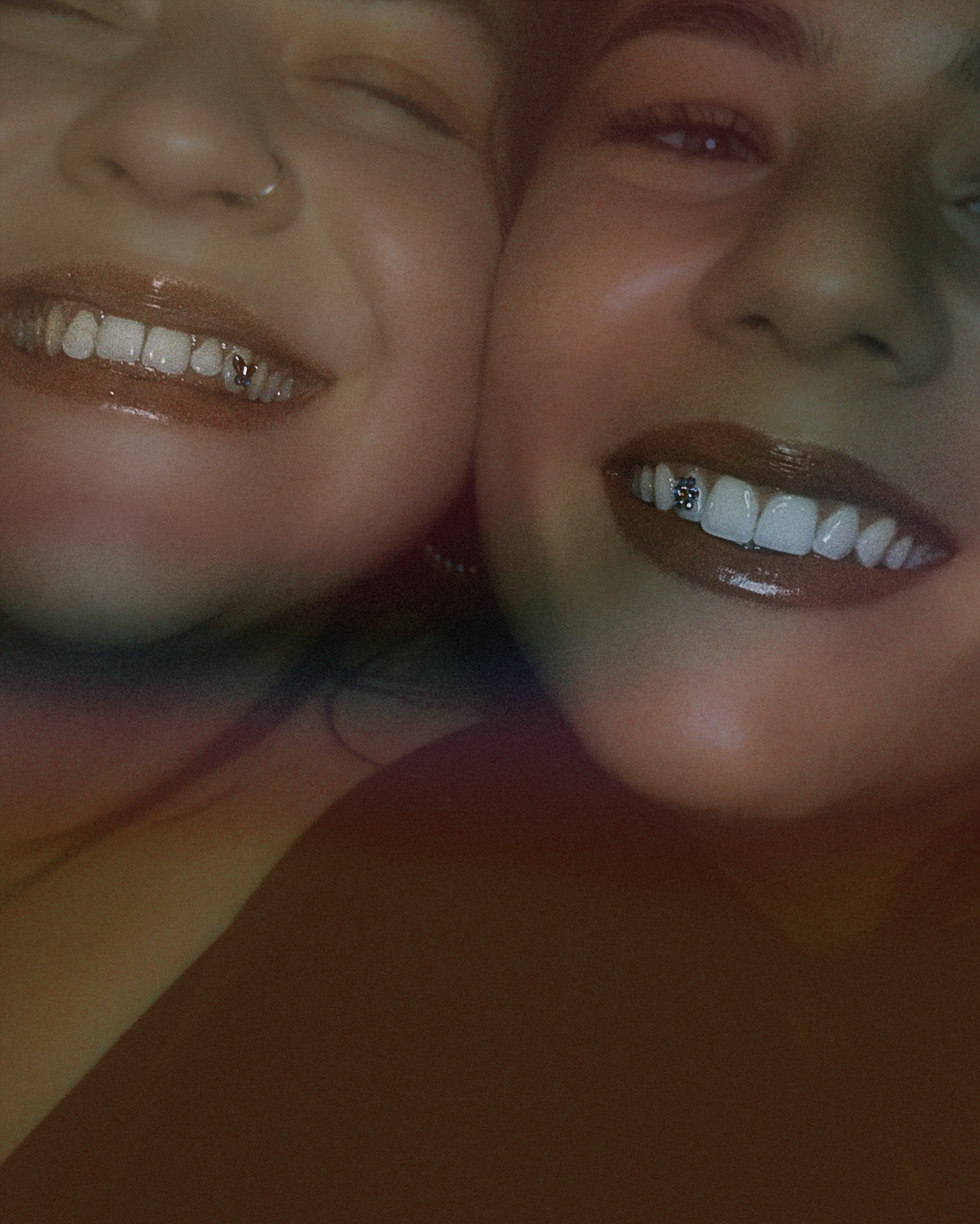 Close-up of two smiling faces of young women with braces, wearing makeup, in an intimate pose.