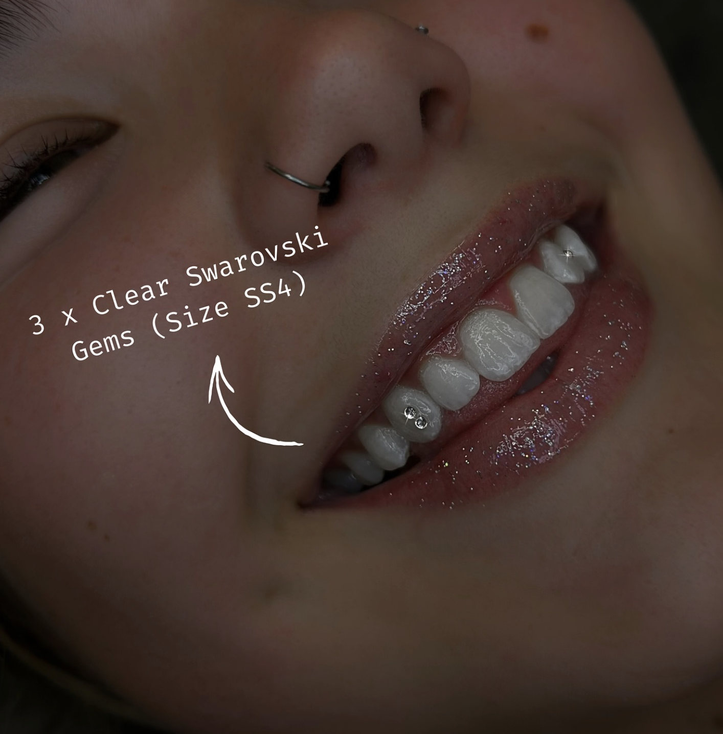 Close-up photo of a person's smile with clear Swarovski gems on their teeth, and a silver nose ring. Text indicates three Swarovski gems of size SS4 on their tooth.