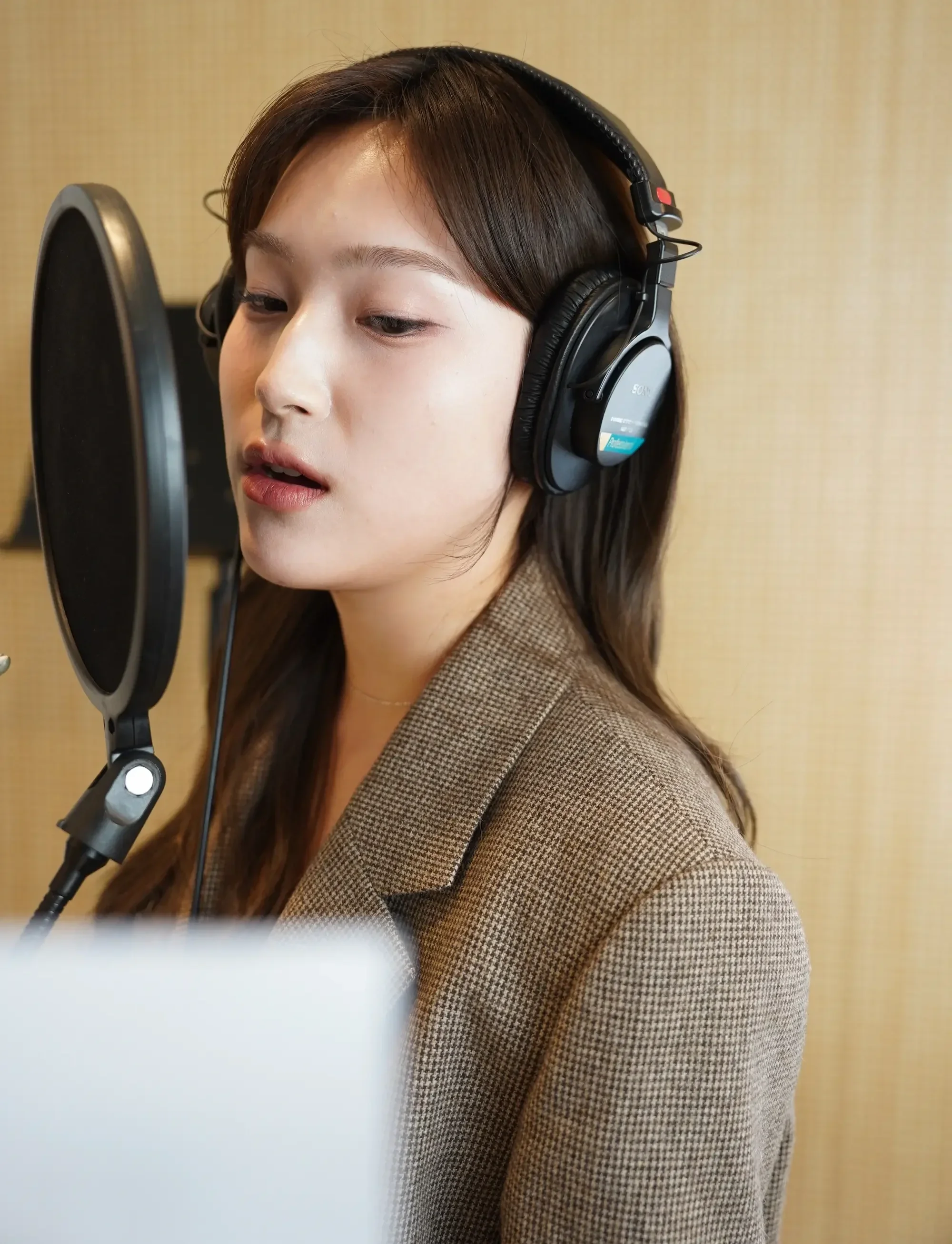 Young woman recording vocals with headphones and a microphone in a studio.