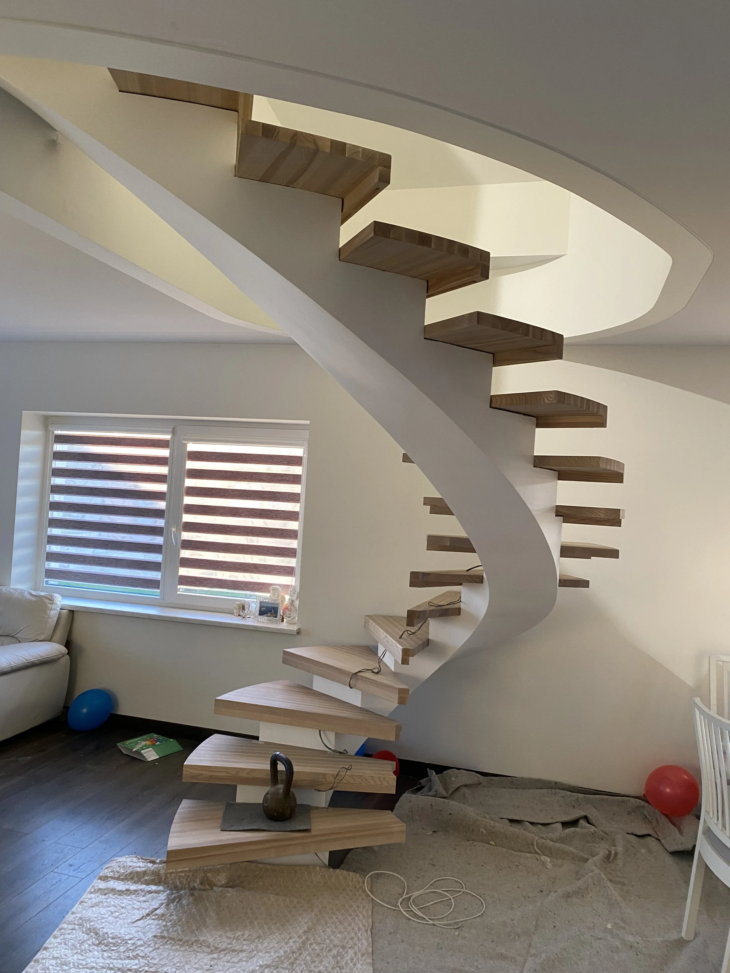 Spiraliniai laiptai iš medinių pakopų ir baltos lenktos atramos.