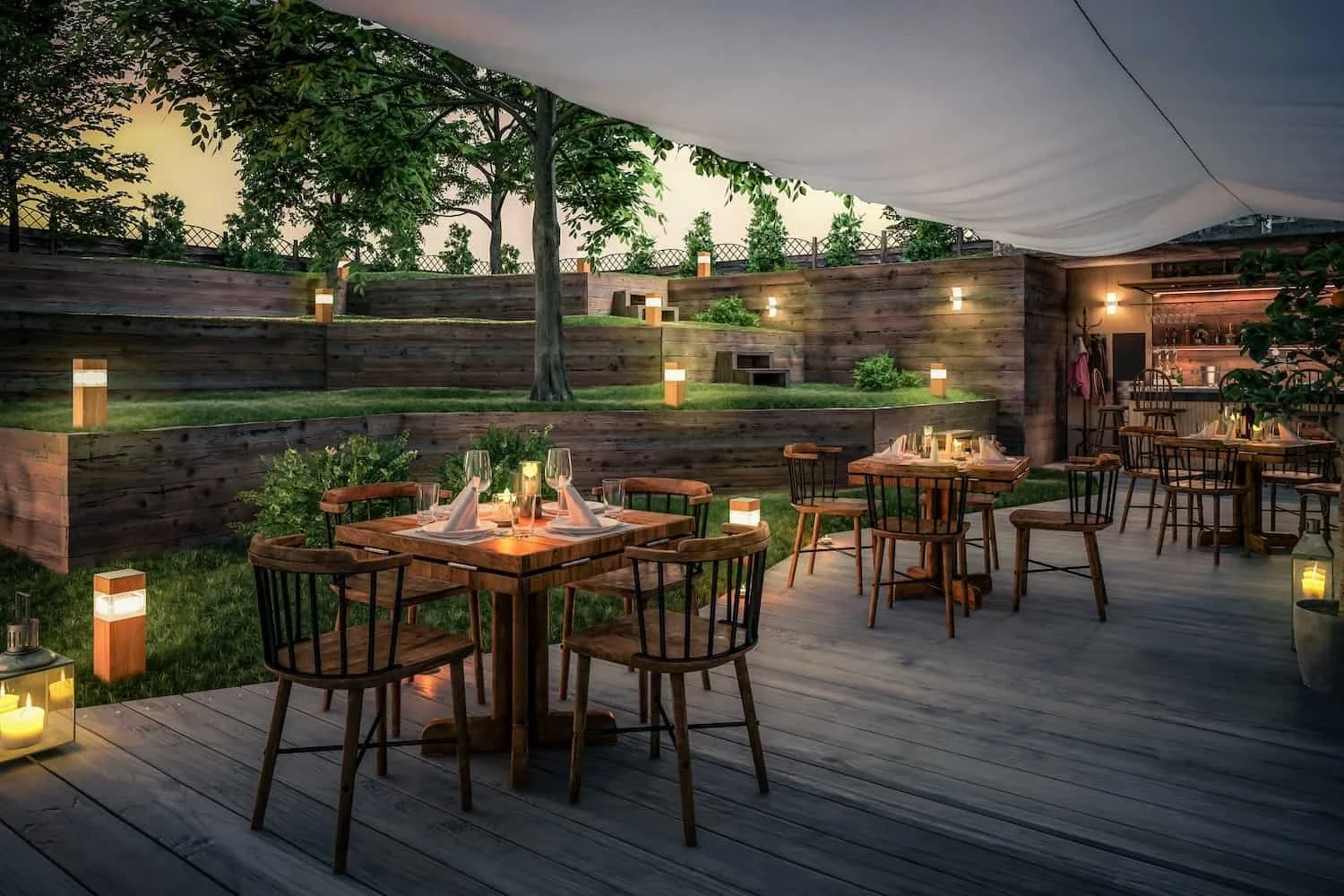Outdoor dining area with wooden tables and chairs, decorated with candles and wine glasses, surrounded by landscaped wooden retaining walls, trees, and soft lighting, creating a cozy ambiance for evening dining.
